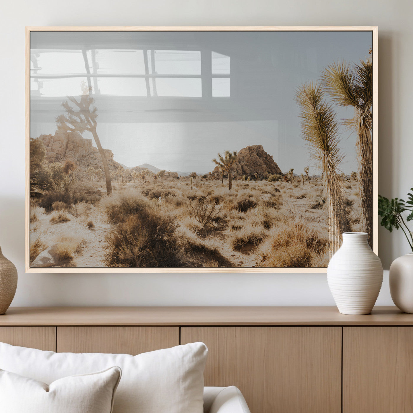 Sunlit desert landscape featuring Joshua trees, rocky formations, and dry bushes under a clear sky.