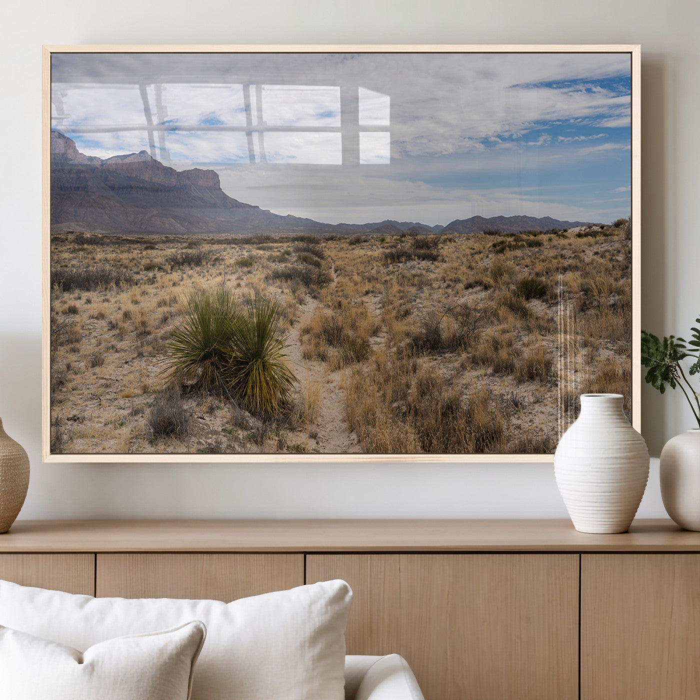 A scenic desert landscape with dry grasses, scattered shrubs, and a distant mountain range under a partly cloudy blue sky.