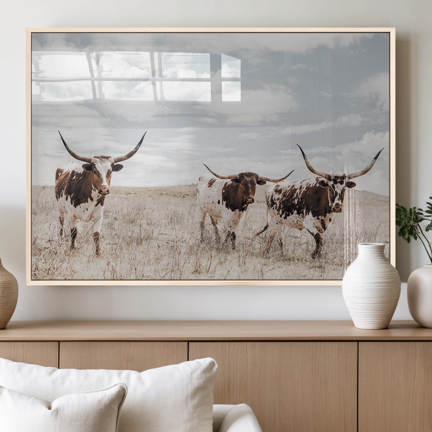 Three Texas Longhorn cattle walking through a dry grassy field under a partly cloudy sky.