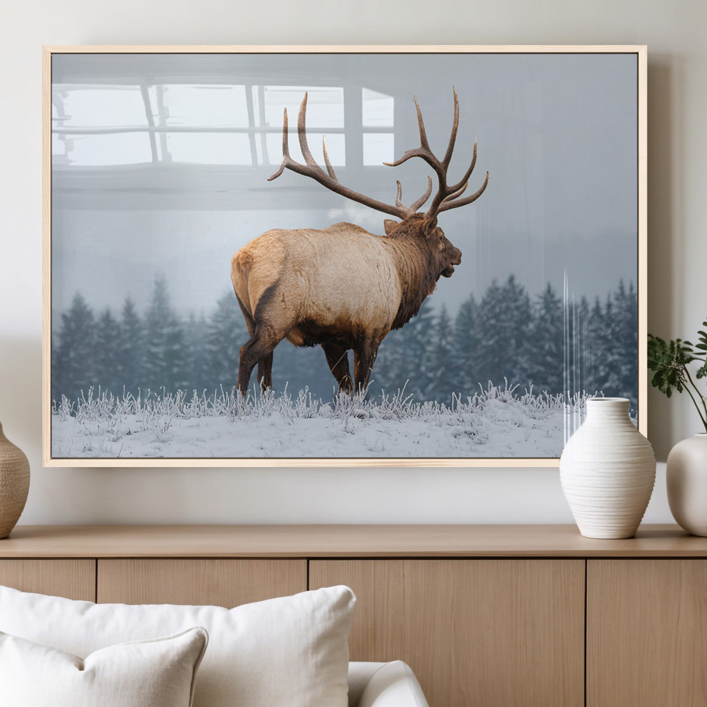 A majestic elk standing in a snowy landscape, with large antlers, set against a backdrop of evergreen trees and a soft winter sky.