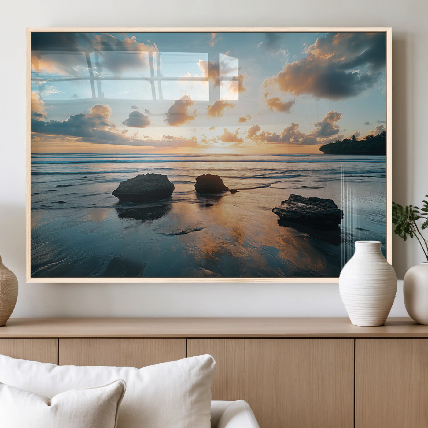 A serene beach at sunset with vibrant clouds, calm water, and rocks in the foreground reflecting the warm colors of the setting sun.