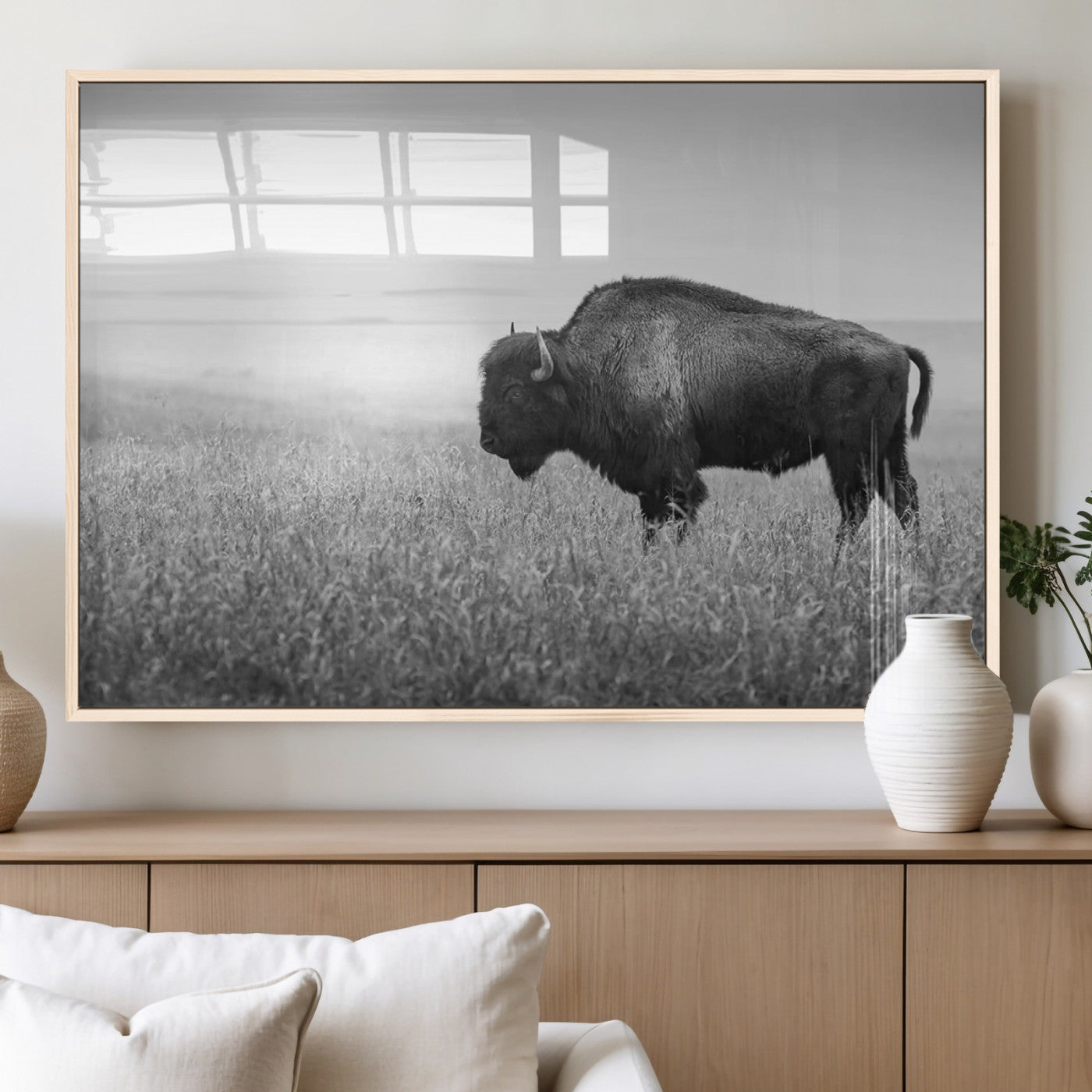 "Black and white image of a bison grazing in a vast field under an overcast sky."