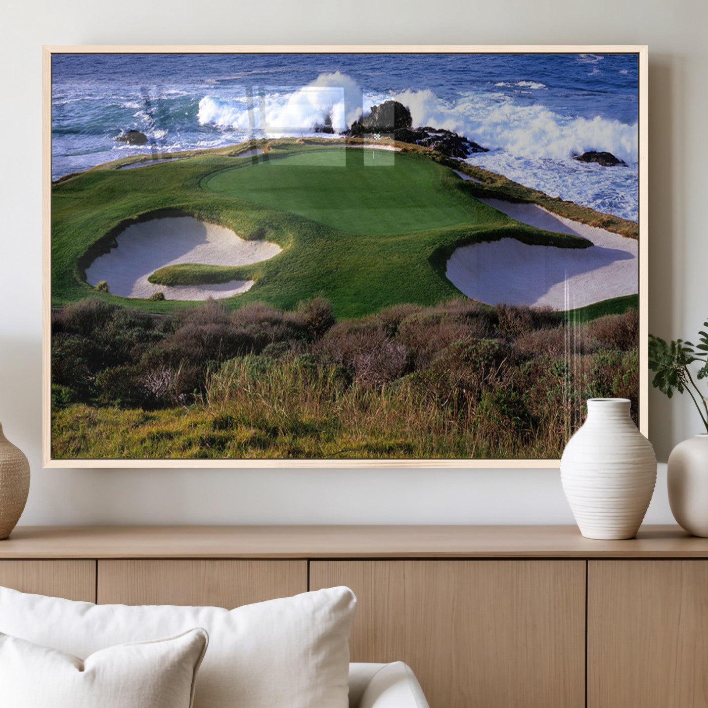 A scenic golf course located by the ocean, featuring a well-manicured green surrounded by sand traps and powerful ocean waves crashing on the shore.