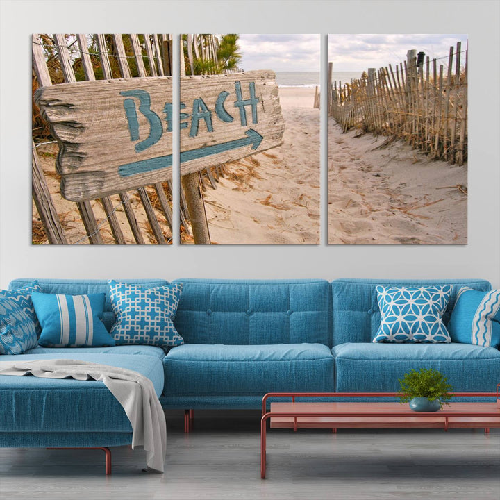 The Beach Is Calling You Wall Art Canvas Print features a sandy beach path with a wooden beach sign and arrow pointing to the ocean, beautifully displayed on museum-quality canvases.