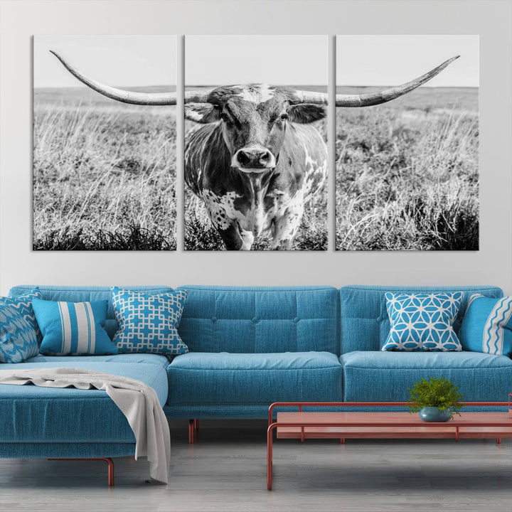 The Texas Cow Longhorn Wall Art Canvas Print is a black and white triptych depicting a cow in a field. It is crafted with museum-quality canvas and features a UV-protective coating.