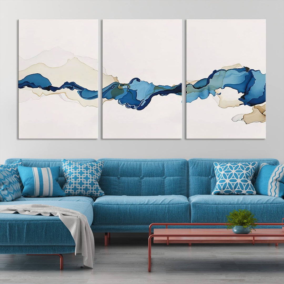 The modern living room showcases a set of three canvas prints with abstract blue art on museum-quality materials.