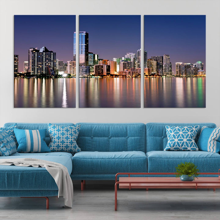 The Miami Skyline Canvas Wall Art Print showcases a vibrant night cityscape and beautifully captures the dazzling colorful lights reflecting on the water. This ready-to-hang triptych adorns the wall, creating a stunning visual centerpiece.