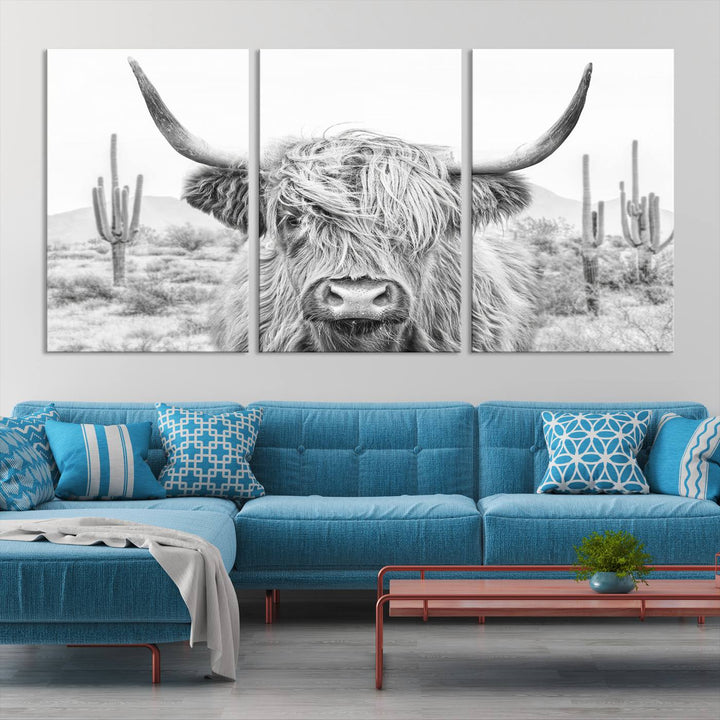 The "Rustic Charm | Cow Longhorn Black White Bighorn Wall Art Canvas Print" is a stunning triptych that showcases a highland cow with long horns set against a desert landscape with cacti in the background. This farmhouse wall art elevates any room into a rustic haven with its gallery-quality canvas.