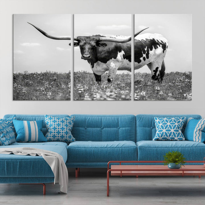 The Texas Black White Highland Longhorn Cow Wall Art Canvas Print, a gallery-quality triptych, elegantly adorns the wall, showcasing a striking black-and-white depiction of a longhorn cow in a field.