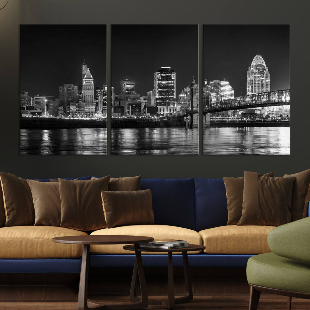 The Cincinnati City Lights Skyline Black and White Wall Art Cityscape Canvas Print elegantly adorns a modern living room. This museum-quality canvas triptych of a city skyline is enhanced by hand-assembled frames for added finesse, and you can enjoy free shipping on this stunning home addition.