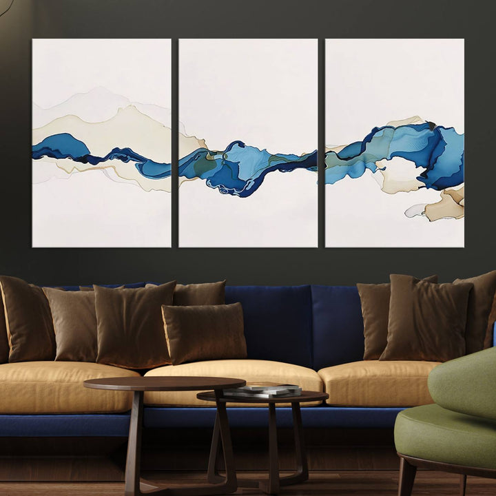 The modern living room showcases a set of three canvas prints with abstract blue art on museum-quality materials.