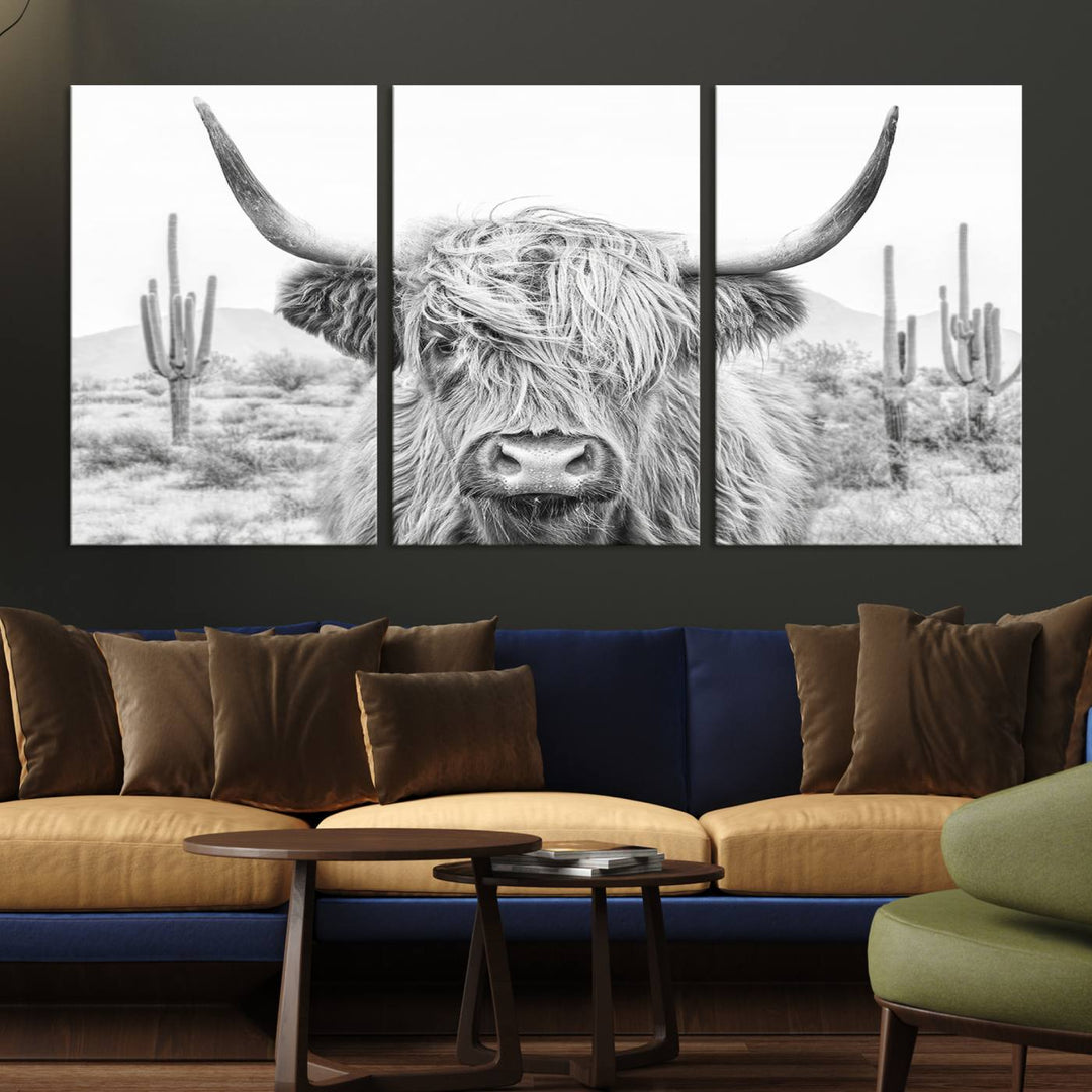 The "Rustic Charm | Cow Longhorn Black White Bighorn Wall Art Canvas Print" is a stunning triptych that showcases a highland cow with long horns set against a desert landscape with cacti in the background. This farmhouse wall art elevates any room into a rustic haven with its gallery-quality canvas.