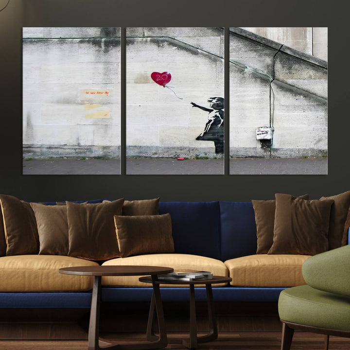 The "Girl with a Balloon Banksy Street Graffiti Art Canvas Print" is a gallery-quality wall art piece that features an image of a girl releasing a heart-shaped balloon. Handmade in the USA, this canvas artwork brings charm and emotion to any room.