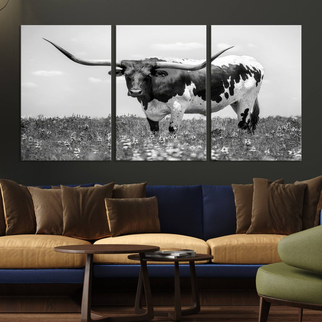 The Texas Black White Highland Longhorn Cow Wall Art Canvas Print, a gallery-quality triptych, elegantly adorns the wall, showcasing a striking black-and-white depiction of a longhorn cow in a field.