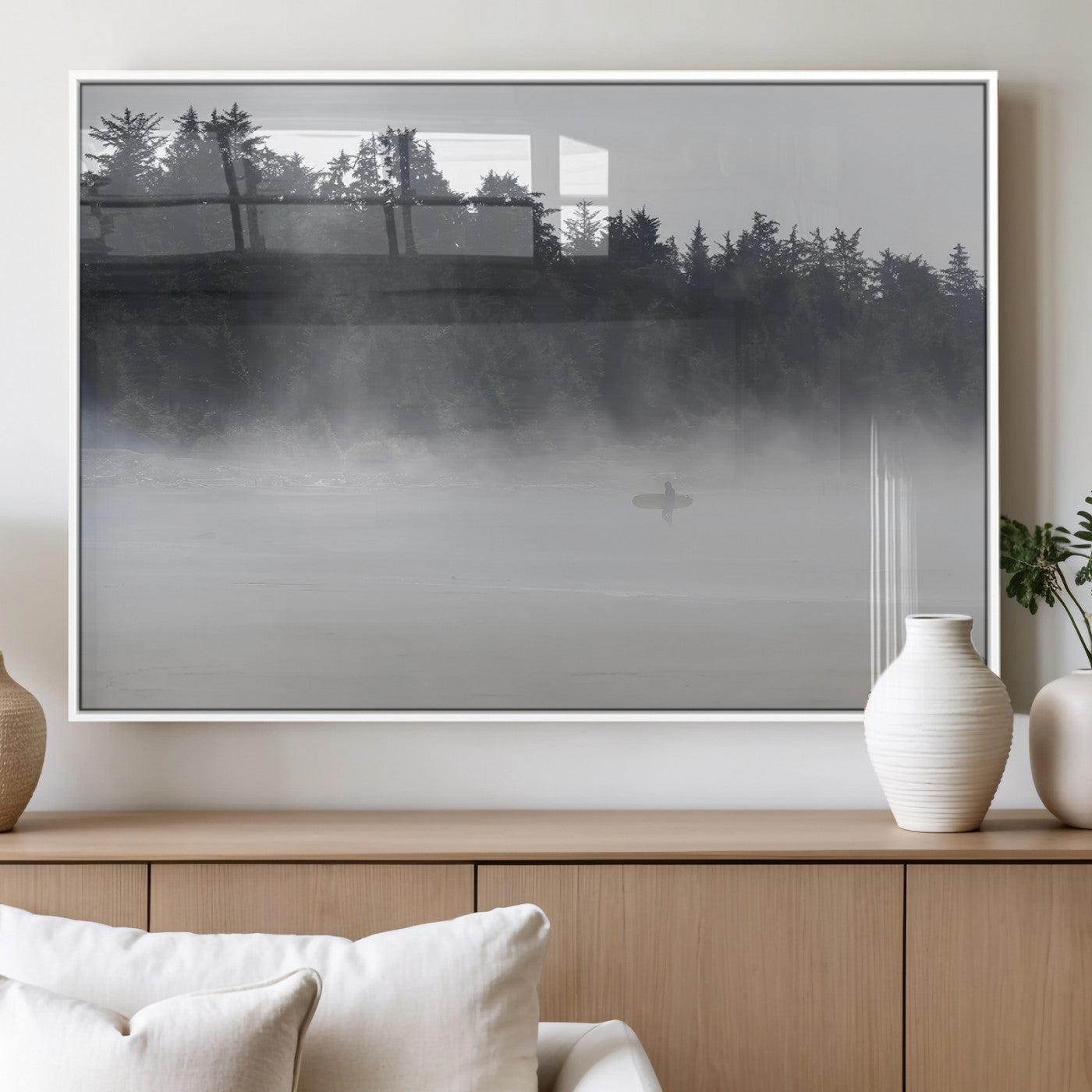 A lone surfer carrying a board through a misty shoreline, surrounded by dense trees and fog, creating a peaceful and mysterious coastal scene.