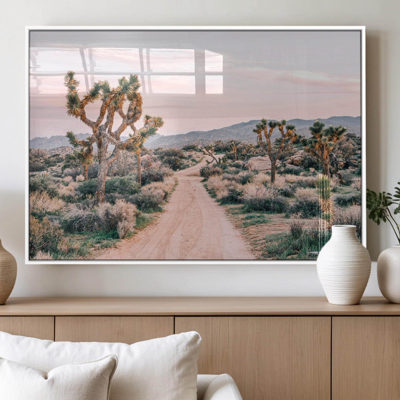 A dusty road winding through Joshua Tree National Park, framed by iconic twisted trees and warm desert tones under a soft pastel sky.