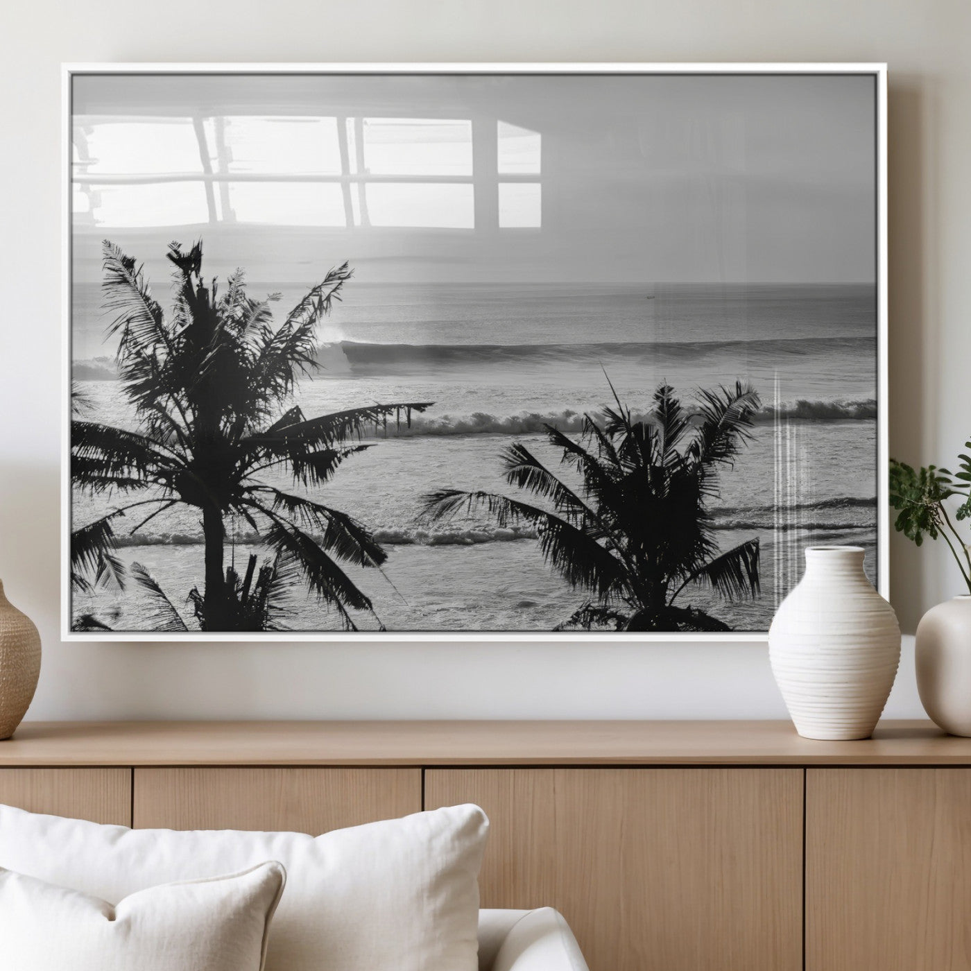 Black and white view of ocean waves crashing on a tropical coastline, framed by silhouetted palm trees under a vast, open sky.
