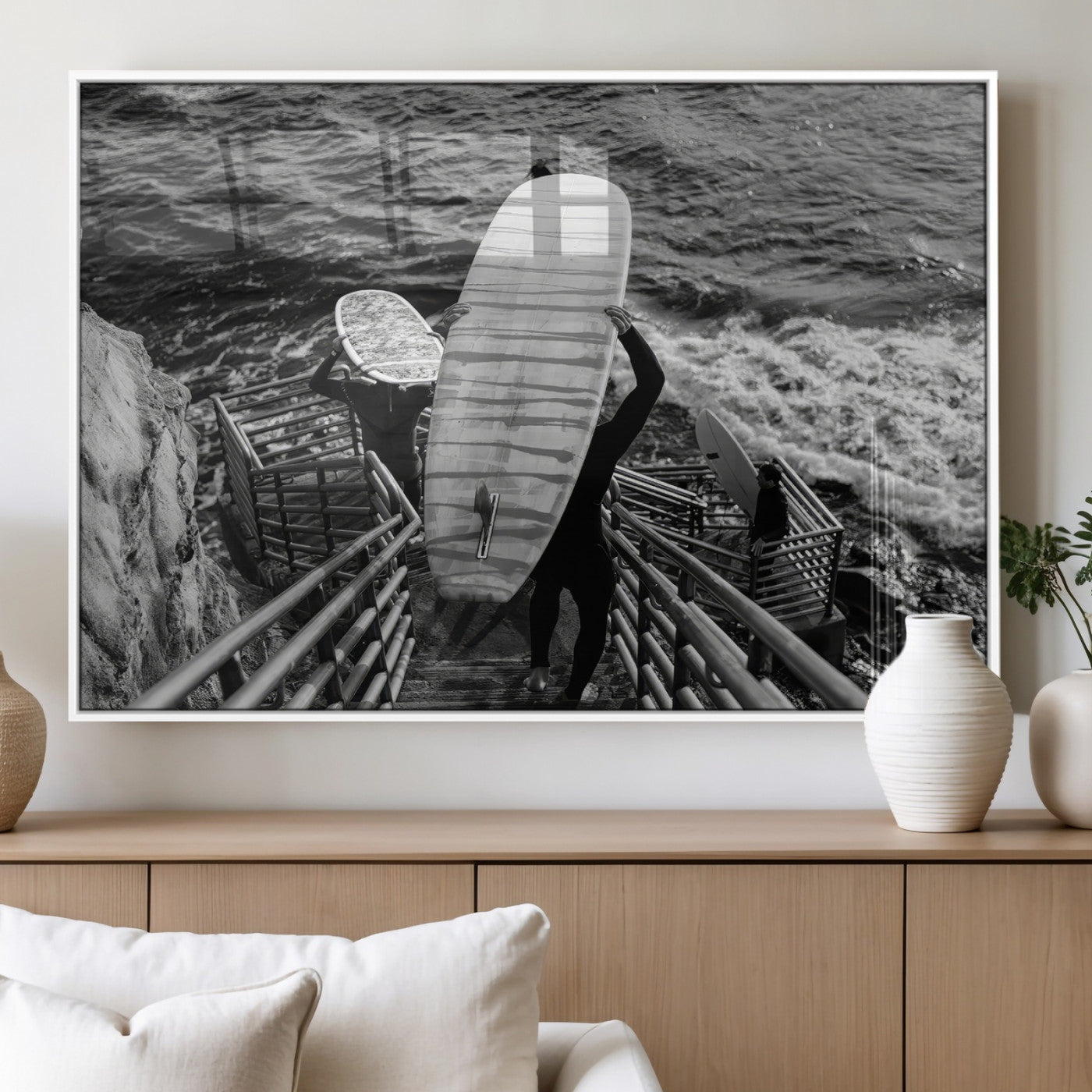 Black and white photo of surfers carrying boards down a rugged cliffside stairway, capturing a bold and adventurous coastal scene.