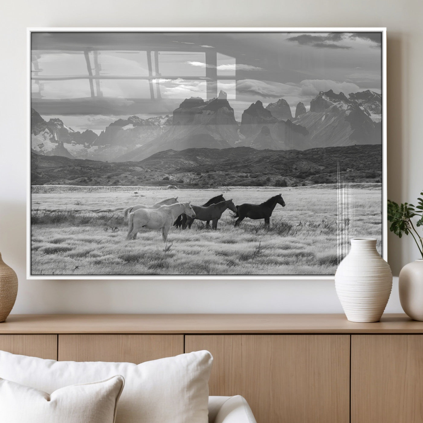 A black and white landscape of wild horses grazing in a vast grassland with towering mountains in the background, creating a moody and rustic western aesthetic.