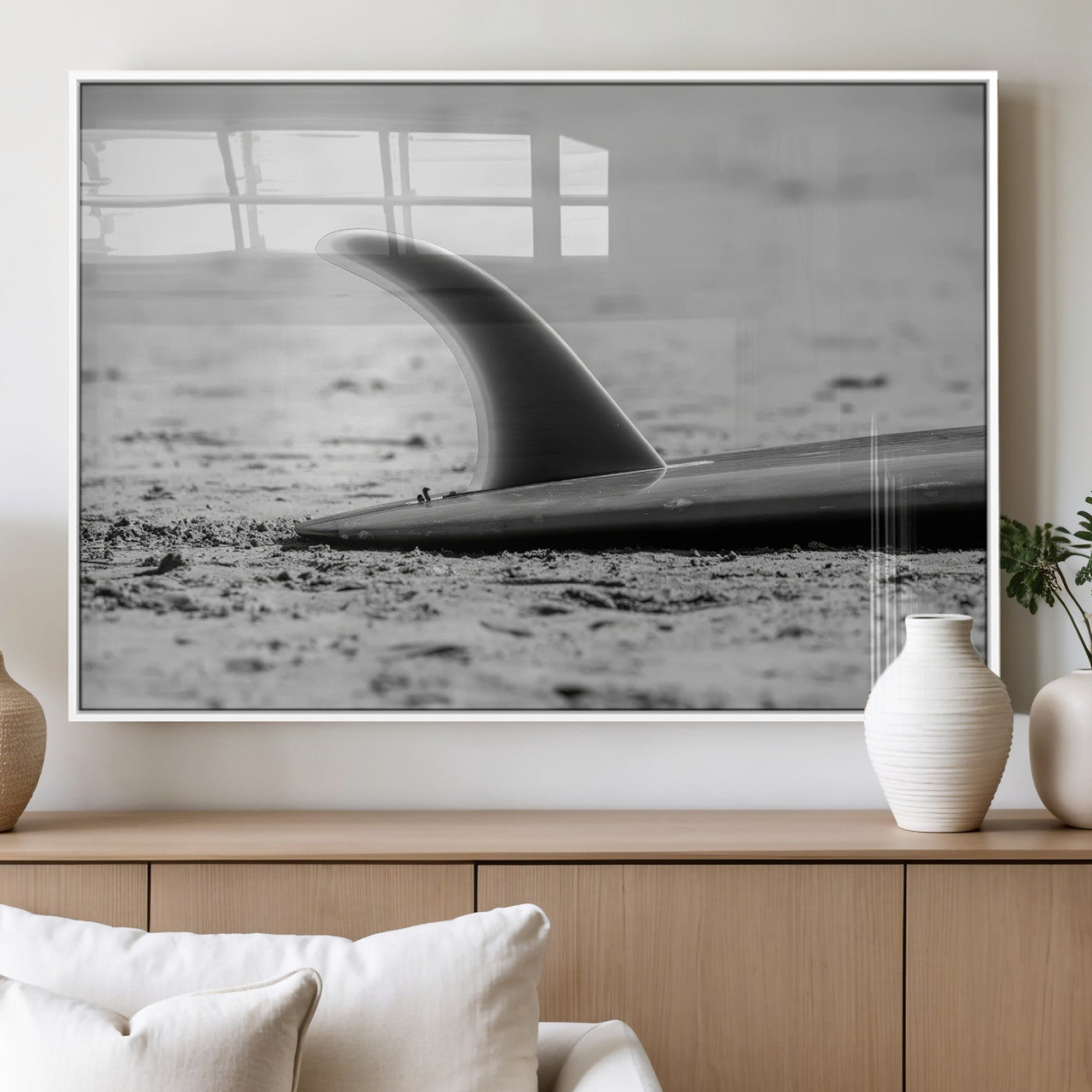 A black and white close-up of a surfboard fin resting on the sandy shore, highlighting minimalist beach aesthetics and classic surf culture.
