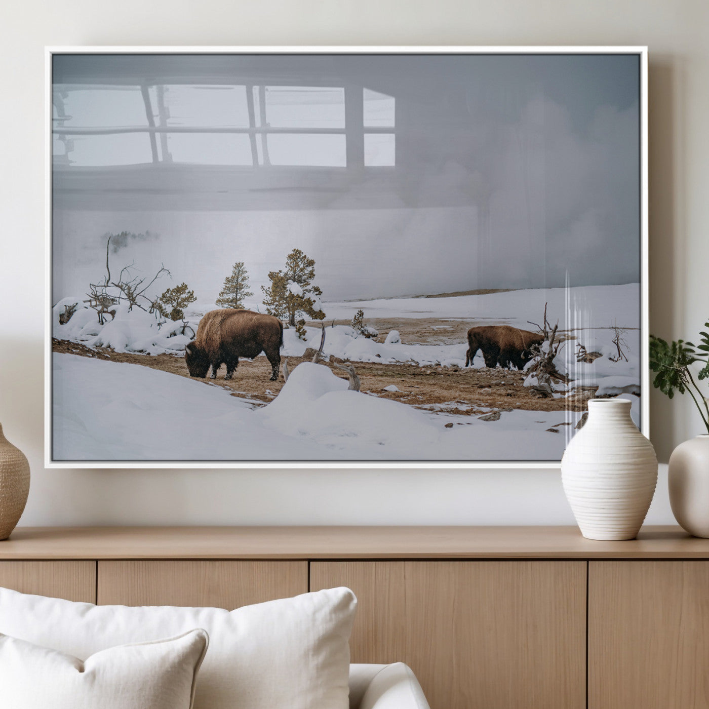 Two bison grazing in a snowy open landscape with misty hills in the background, creating a peaceful and rustic winter scene.