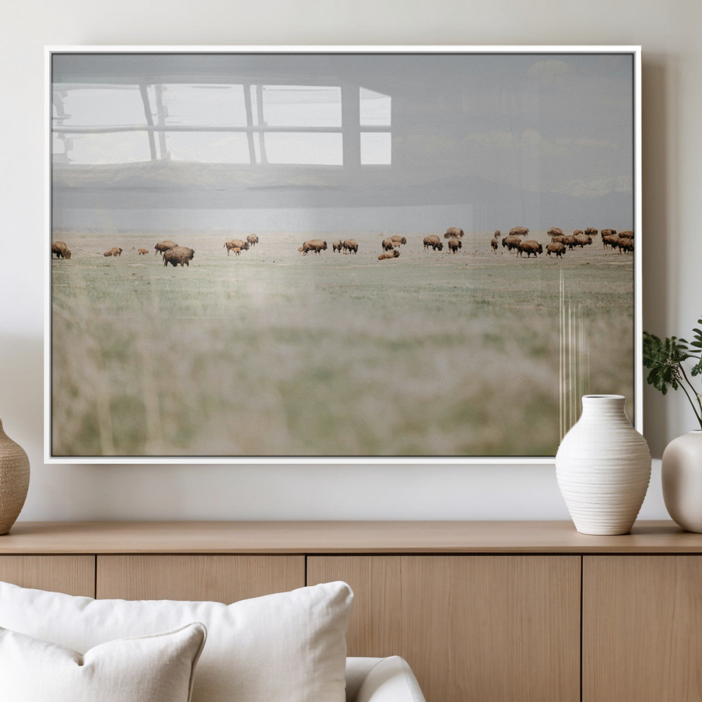 A herd of bison grazing in an open prairie with distant mountains under a soft sky, creating a serene and rustic Western landscape.