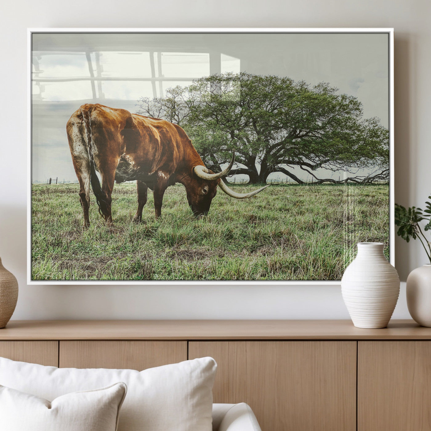 A Texas Longhorn grazing in a green pasture with a large tree in the background, evoking a rustic Western and farmhouse aesthetic.