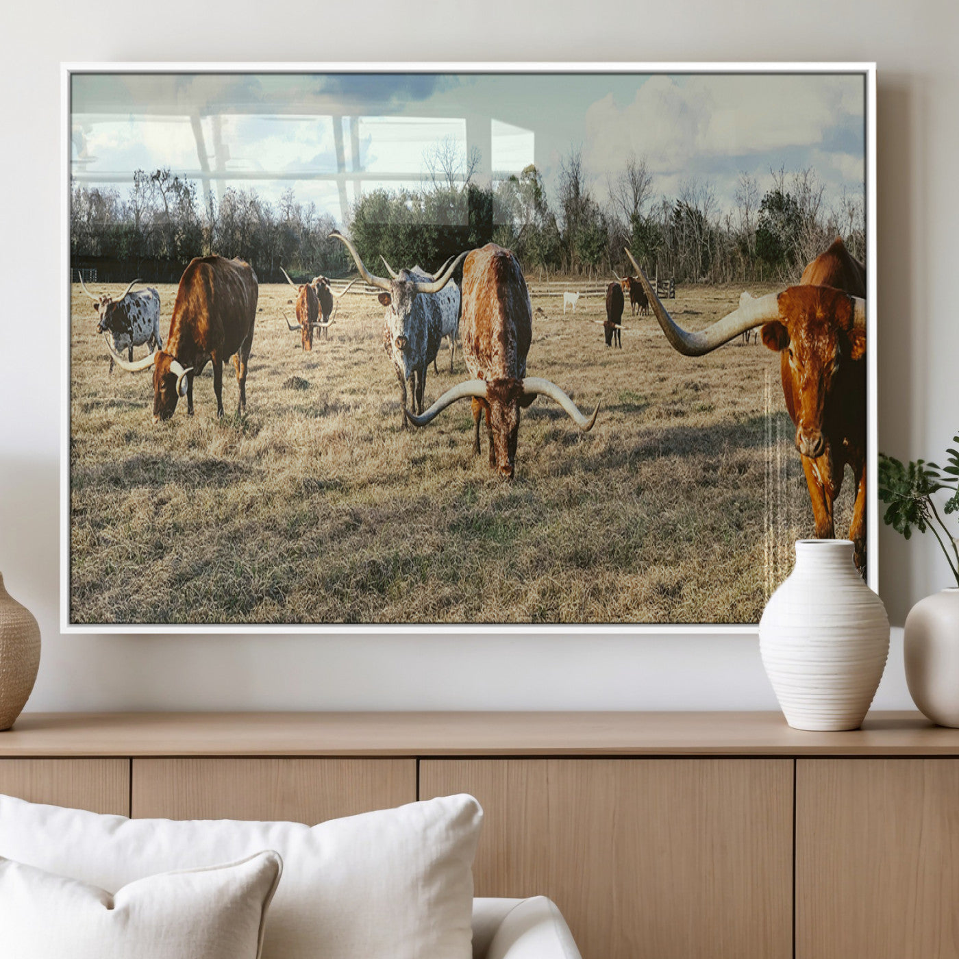 A herd of Texas Longhorn cattle grazing in an open field under a partly cloudy sky, capturing a rustic and Western ranch aesthetic.