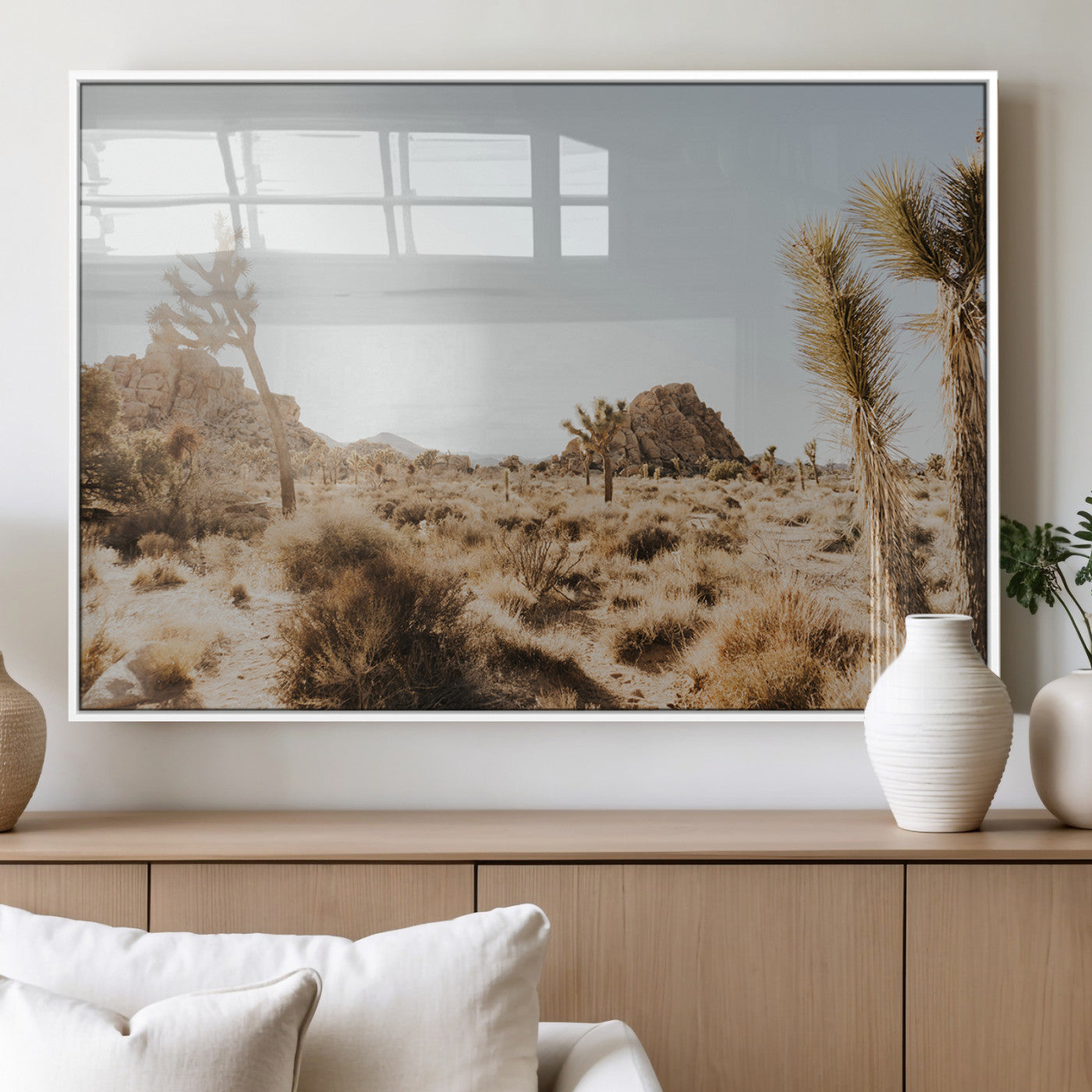 Sunlit desert landscape featuring Joshua trees, rocky formations, and dry bushes under a clear sky.