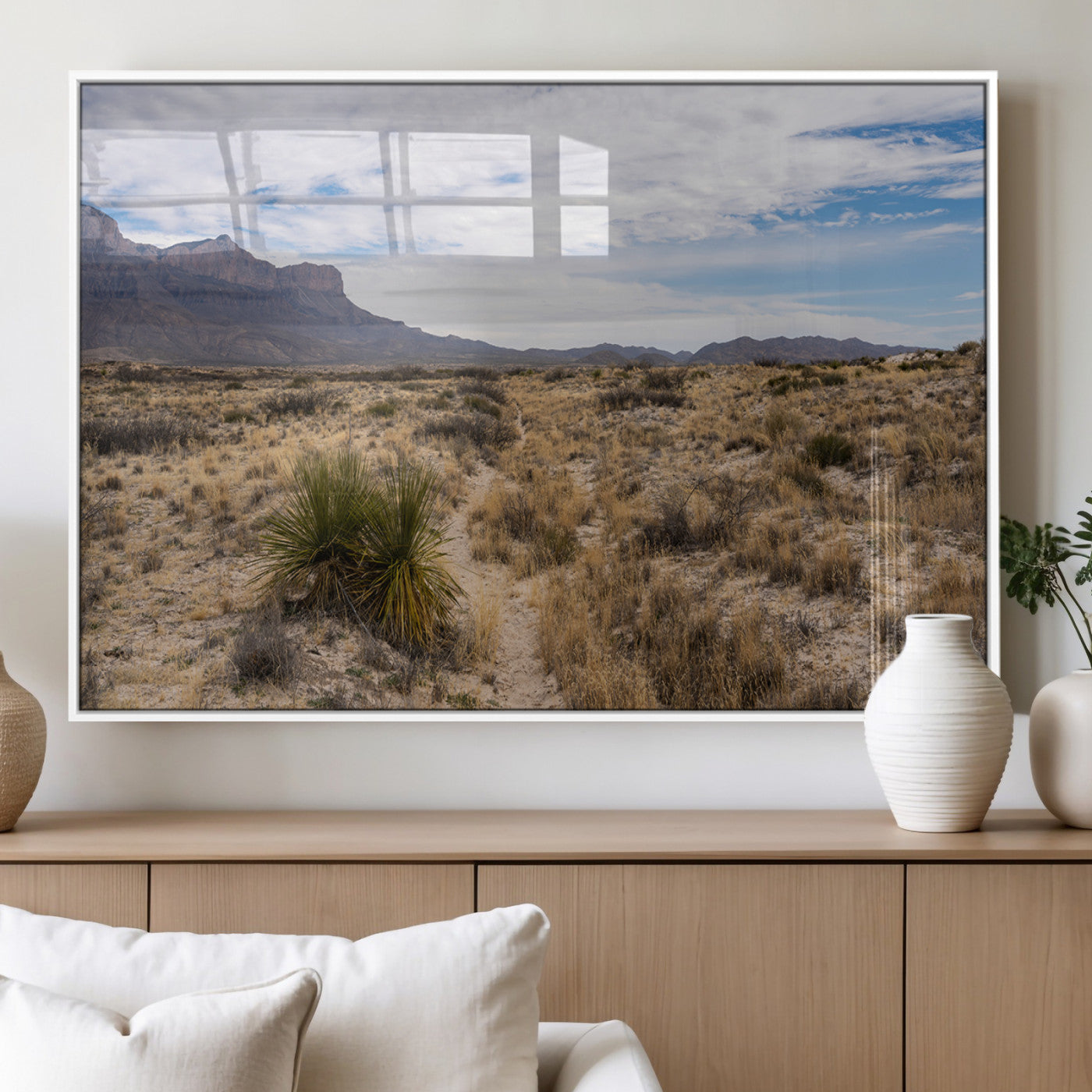 A scenic desert landscape with dry grasses, scattered shrubs, and a distant mountain range under a partly cloudy blue sky.