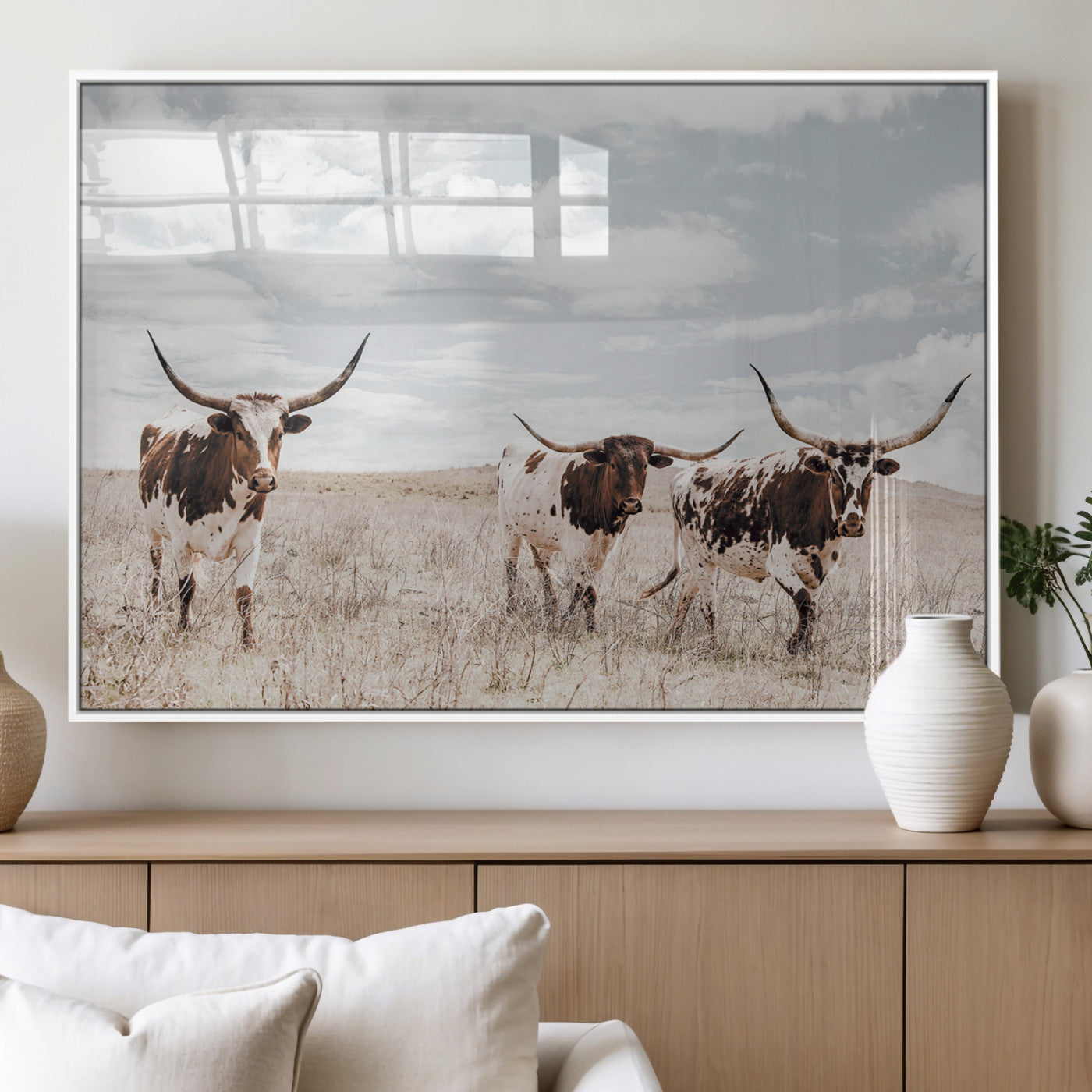 Three Texas Longhorn cattle walking through a dry grassy field under a partly cloudy sky.