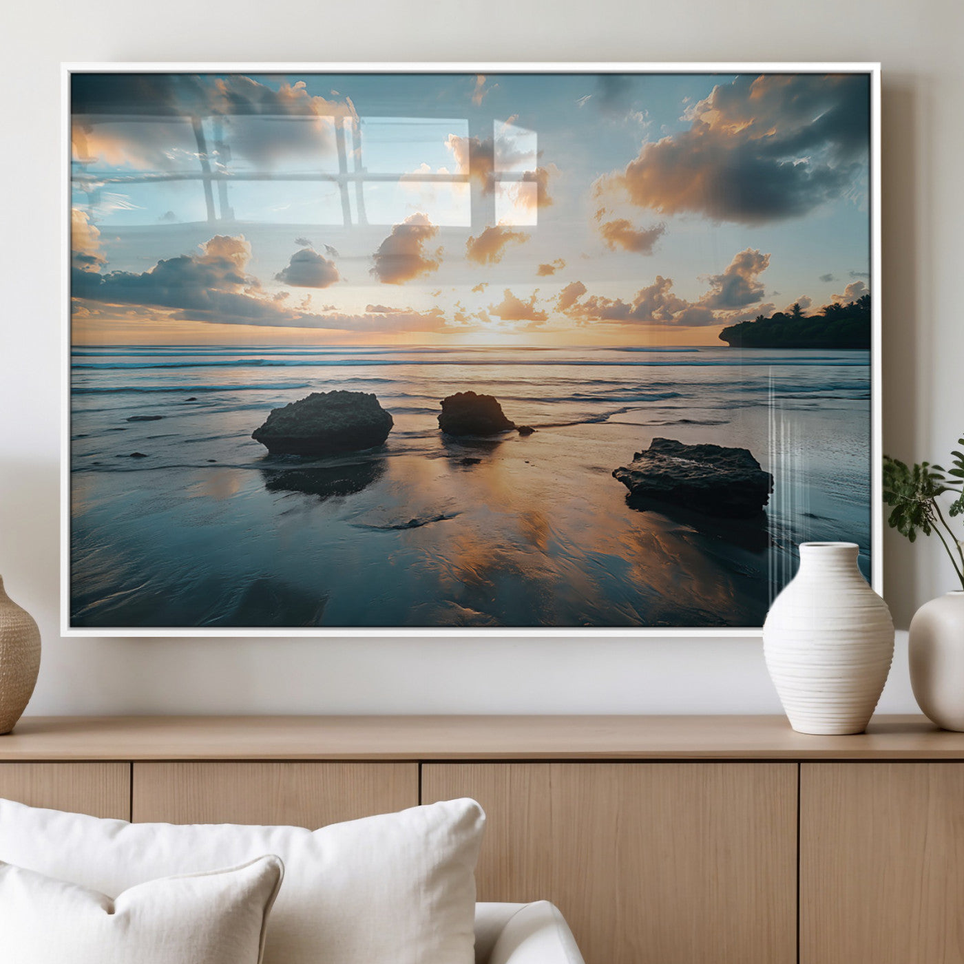 A serene beach at sunset with vibrant clouds, calm water, and rocks in the foreground reflecting the warm colors of the setting sun.