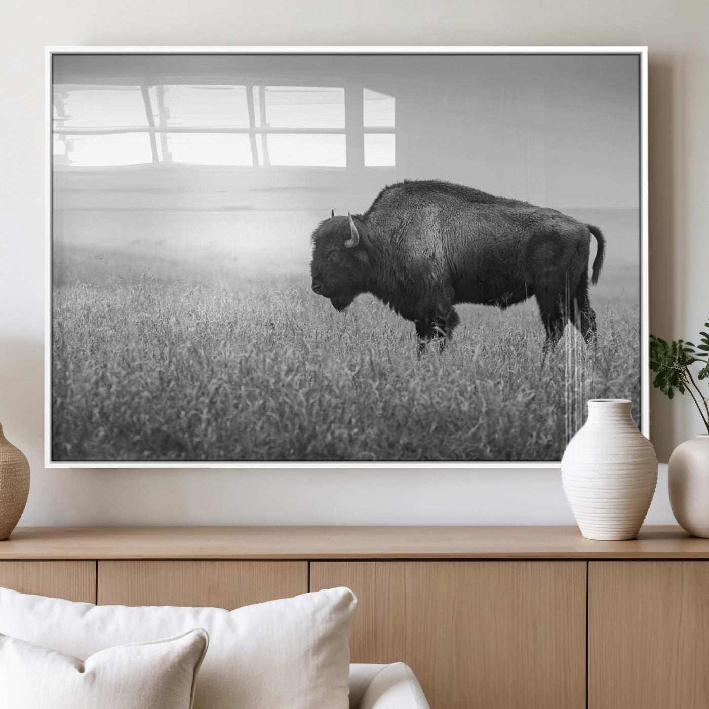 "Black and white image of a bison grazing in a vast field under an overcast sky."