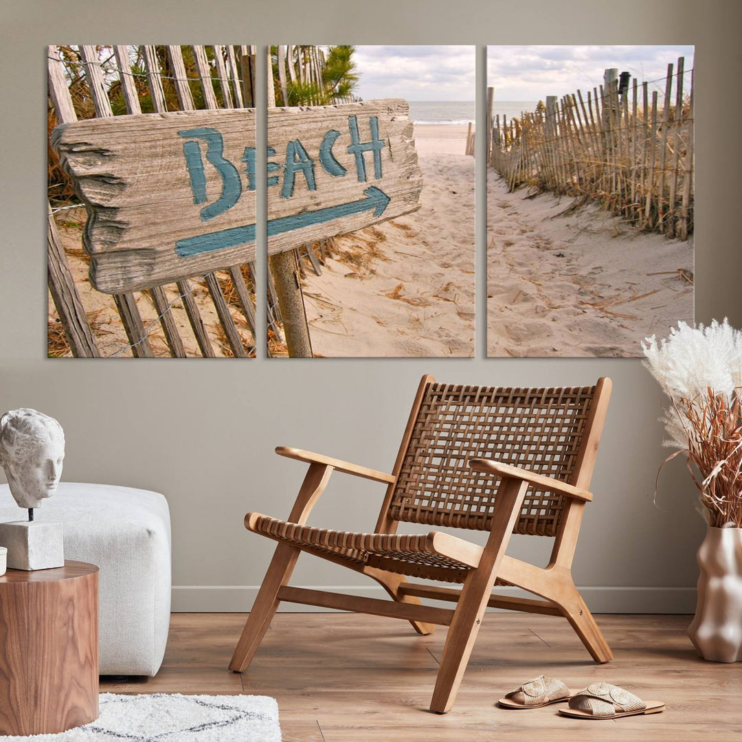 The Beach Is Calling You Wall Art Canvas Print features a sandy beach path with a wooden beach sign and arrow pointing to the ocean, beautifully displayed on museum-quality canvases.