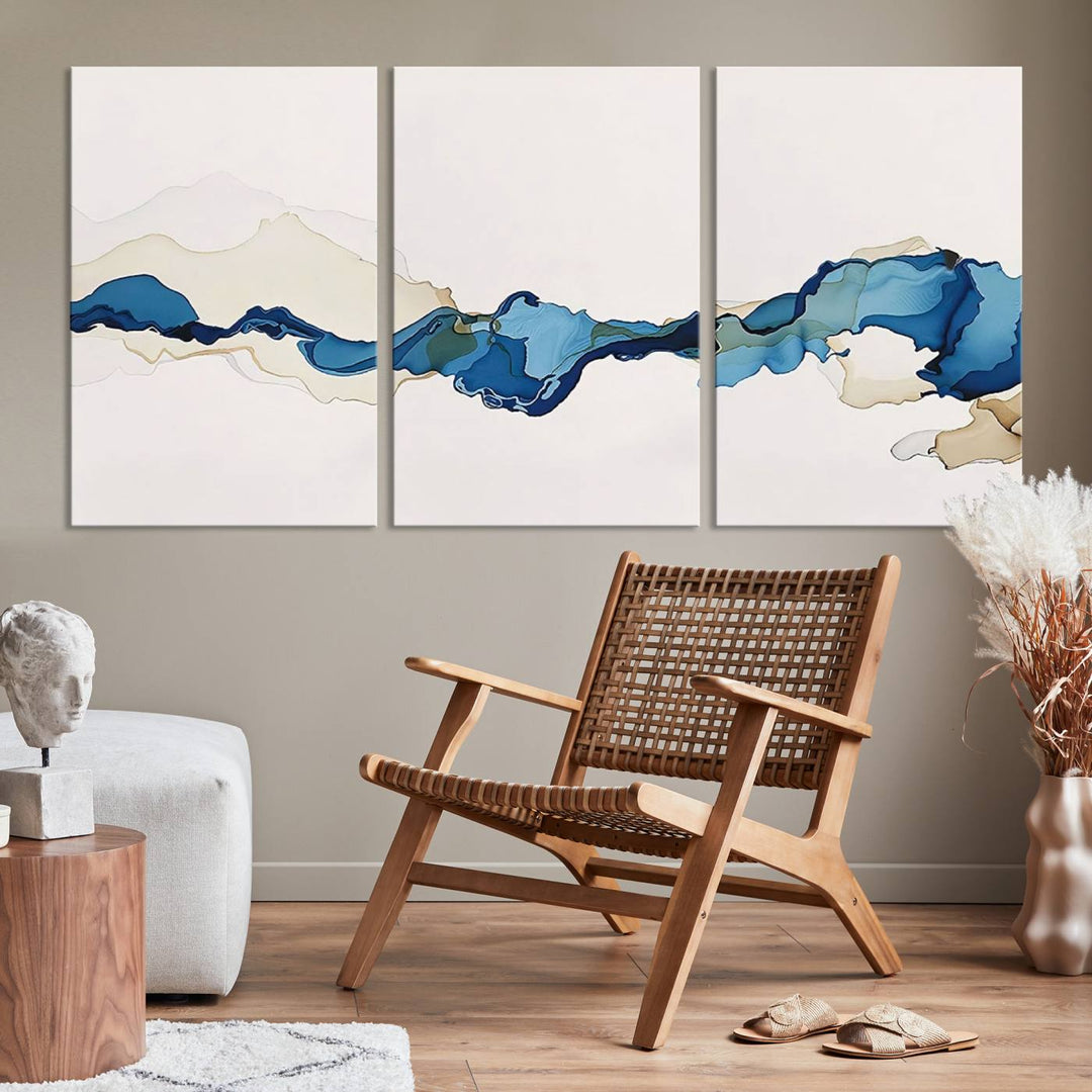 The modern living room showcases a set of three canvas prints with abstract blue art on museum-quality materials.