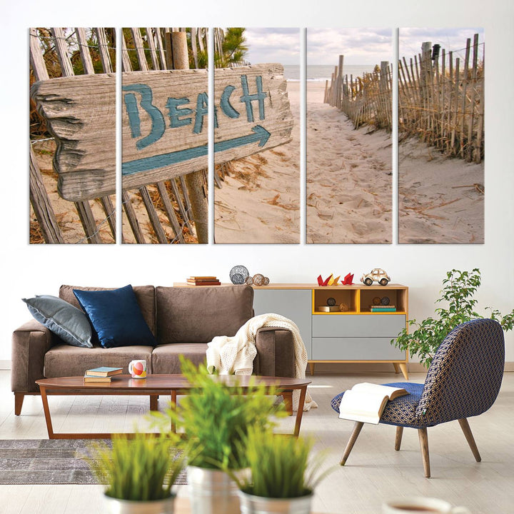 The Beach Is Calling You Wall Art Canvas Print features a sandy beach path with a wooden beach sign and arrow pointing to the ocean, beautifully displayed on museum-quality canvases.