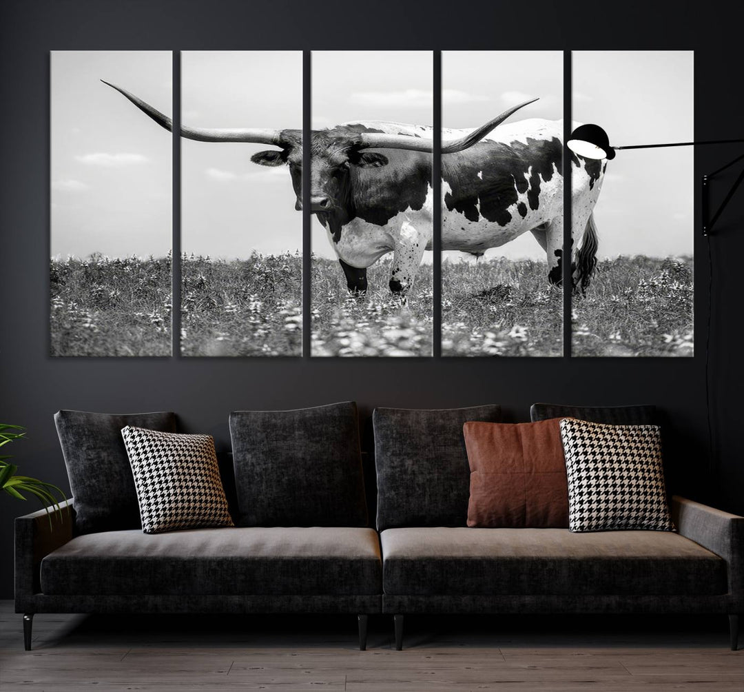 The Texas Black White Highland Longhorn Cow Wall Art Canvas Print, a gallery-quality triptych, elegantly adorns the wall, showcasing a striking black-and-white depiction of a longhorn cow in a field.