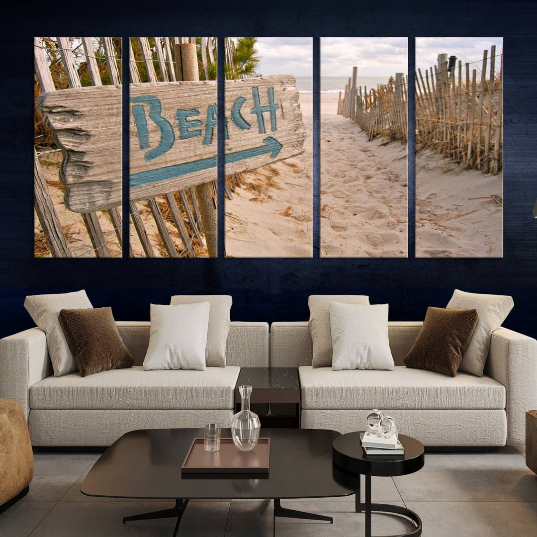 The Beach Is Calling You Wall Art Canvas Print features a sandy beach path with a wooden beach sign and arrow pointing to the ocean, beautifully displayed on museum-quality canvases.