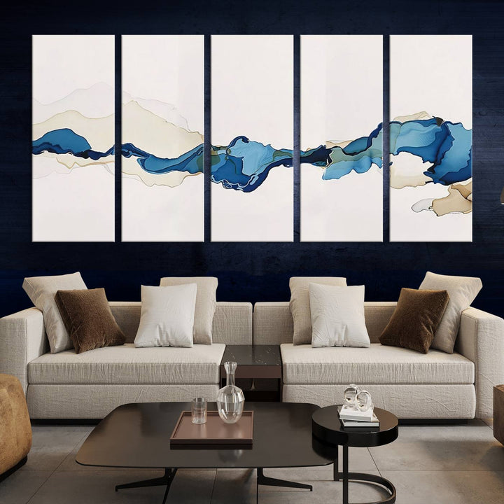 The modern living room showcases a set of three canvas prints with abstract blue art on museum-quality materials.