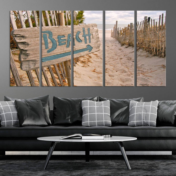 The Beach Is Calling You Wall Art Canvas Print features a sandy beach path with a wooden beach sign and arrow pointing to the ocean, beautifully displayed on museum-quality canvases.