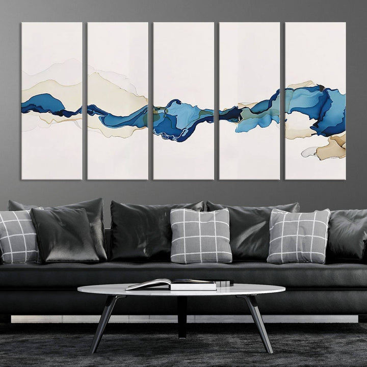 The modern living room showcases a set of three canvas prints with abstract blue art on museum-quality materials.