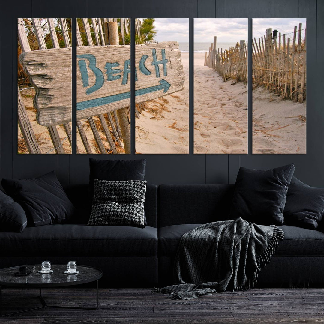 The Beach Is Calling You Wall Art Canvas Print features a sandy beach path with a wooden beach sign and arrow pointing to the ocean, beautifully displayed on museum-quality canvases.