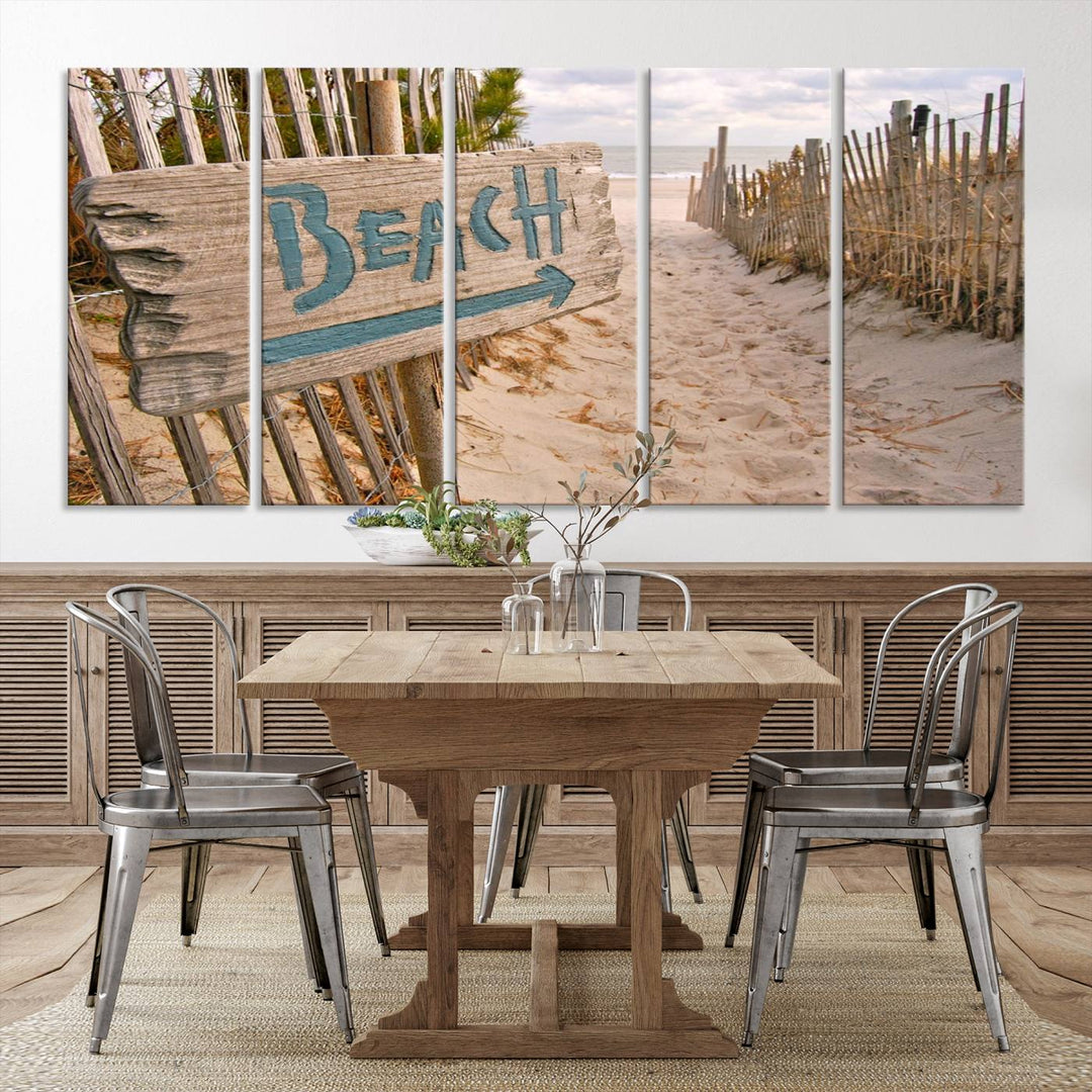 The Beach Is Calling You Wall Art Canvas Print features a sandy beach path with a wooden beach sign and arrow pointing to the ocean, beautifully displayed on museum-quality canvases.