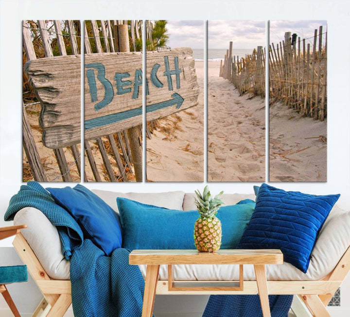 The Beach Is Calling You Wall Art Canvas Print features a sandy beach path with a wooden beach sign and arrow pointing to the ocean, beautifully displayed on museum-quality canvases.