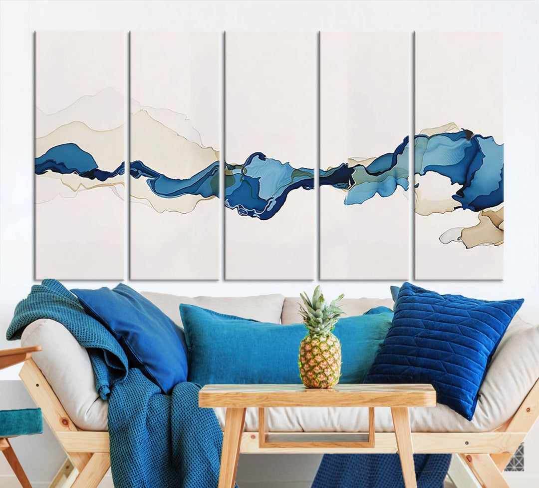 The modern living room showcases a set of three canvas prints with abstract blue art on museum-quality materials.