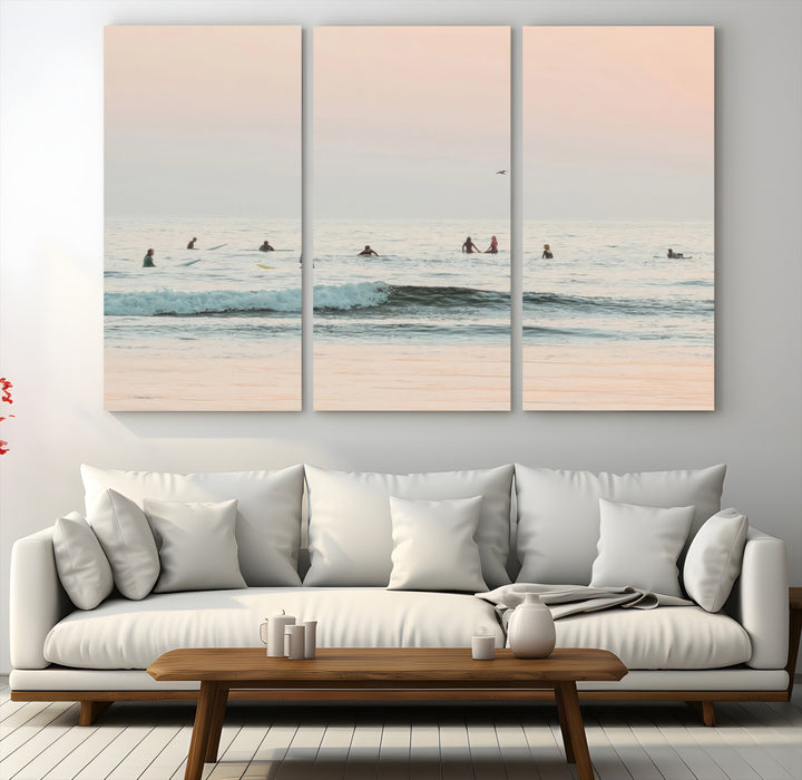 Dreamy photo of surfers waiting on soft pastel waves under a pink sunset sky, ideal for soft coastal minimalist or serene ocean-themed home decor.