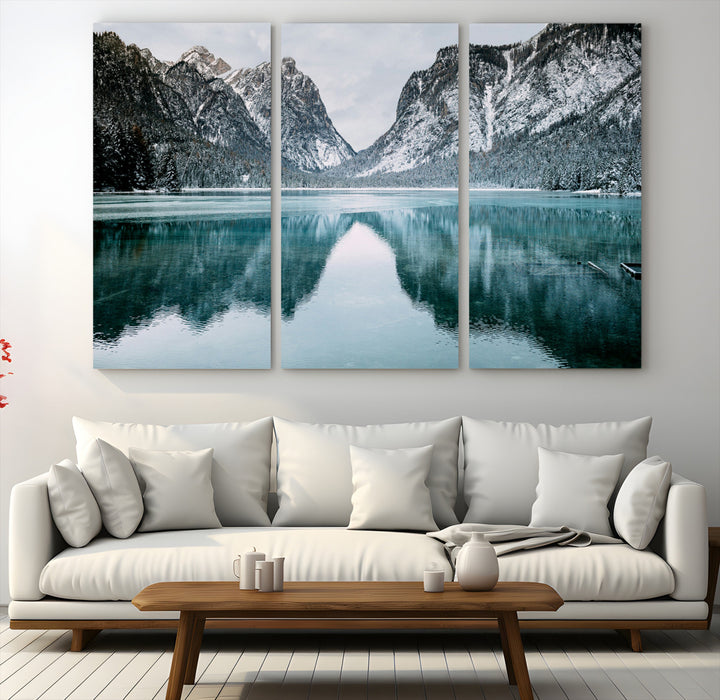 Crystal-clear alpine lake reflecting snow-covered mountains, surrounded by evergreen trees, creating a serene and tranquil winter landscape.