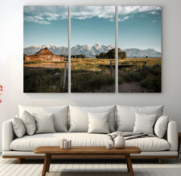 A rustic farmhouse with a wooden barn set against majestic mountain peaks under a soft blue sky, evoking peaceful countryside charm.