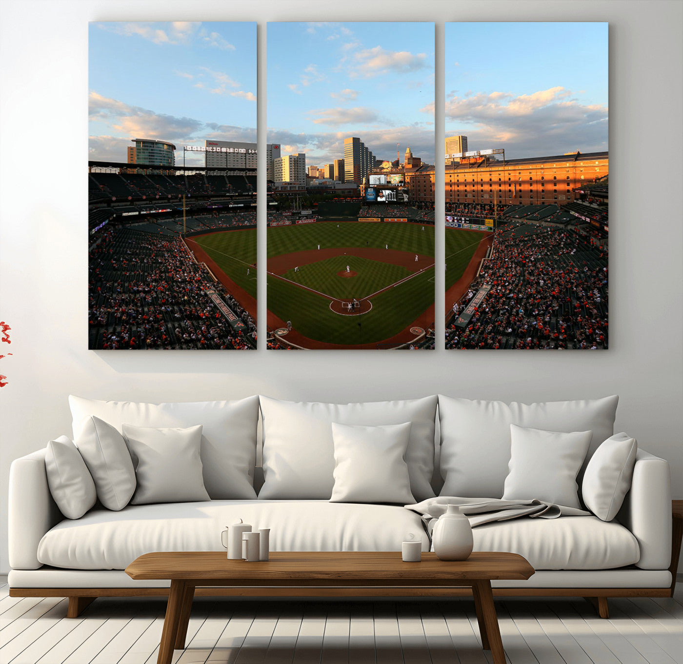 Aerial view of a baseball stadium at sunset with players on the field, fans in the stands, a city skyline in the background, and the setting sun casting warm light on the buildings.