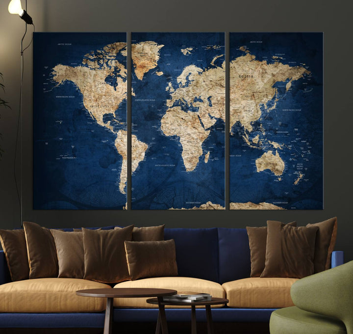 A large framed world map canvas print features beige landmasses set against a grunge-stained deep blue ocean background, creating an intriguing piece of wall art.